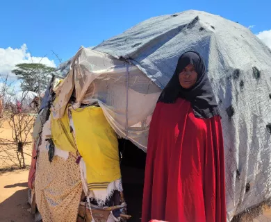 Kenya_Woman in red dress and black hijab standing in front on makeshift shelter at Dadaab