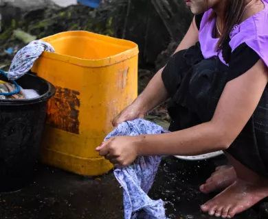 Myanmar_Woman in purple shirt hand washing next to yellow water can