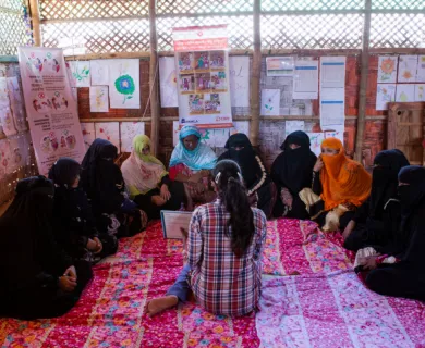 Rohingya_Women in niqabs sitting on the floor while other lady explains lesson from a book