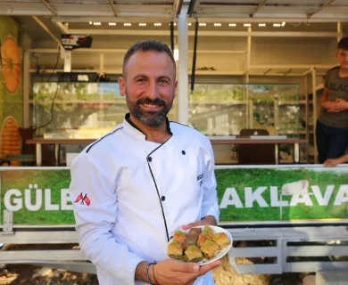 Turkiye_Man in chef jacket standing in front of food truck holding baklava
