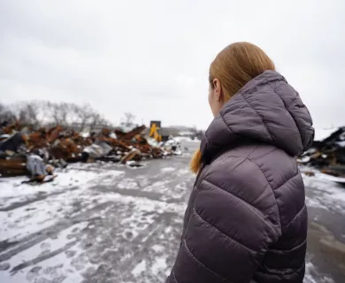 Lateral view of woman with grey winter jacket looking at street with snow and rubble