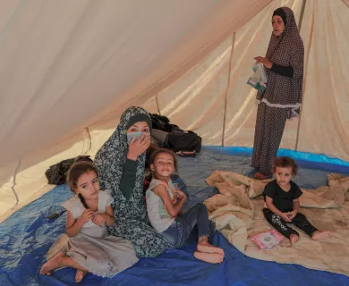 Woman with surgical mask sitting on the floor of a tent with three children