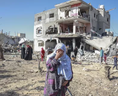 Palestinian woman covering her face in despair in front of a destroyed building.
