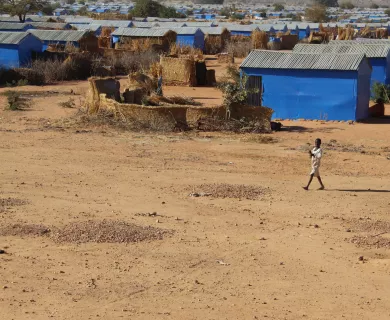 Child walking in dirt field with blue shelters in the background