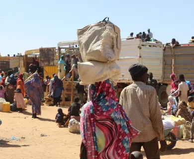 Woman's back carrying bags on her head in an arid space with spread out people