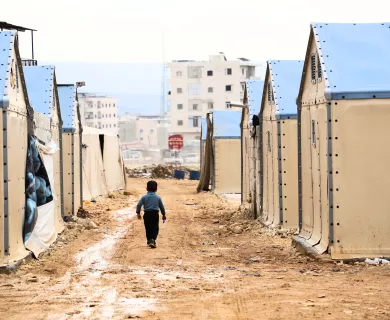 Boy walking in dirt road filled with tents