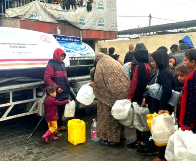 People with plastic bottles line up in front of water truck