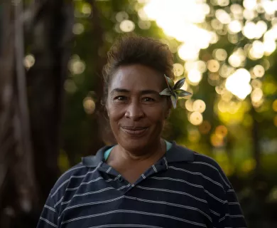 Woman with timid smile with hair up and flower on the ear with forest in the background