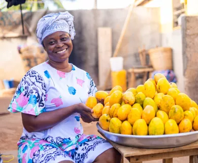 Woman wearing patterned outfit, sitting on bench, showing pile of lemons over metal tray