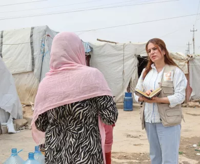 Back of woman wearing pink scarf in front of woman with notebook making notes, wearing CARE's vest