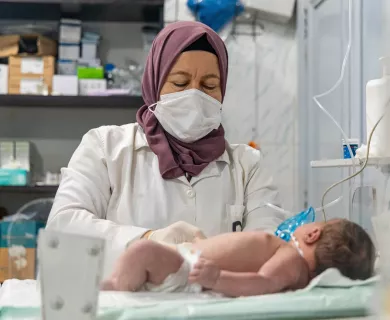 Nurse with purple scarf caring for baby lying on gurney