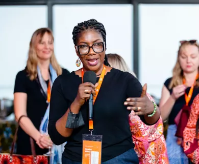 Woman with glasses wearing black t-shirt speaking on microphone