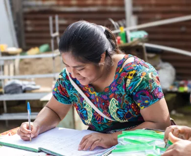 Woman wearing patterned t-shirt writing on notebook.