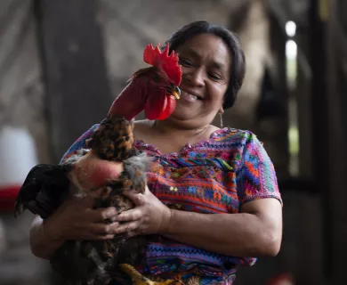 Woman wearing patterned dress smiling while holding a chicken