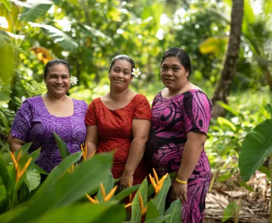 Three women wearing patterned dresses smiling at the camera while standing in a green area